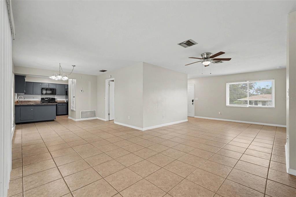 An open-concept living and dining area features beige tile flooring and a dark gray kitchen — 7170 HOLIDAY DRIVE, SPRING HILL, FL