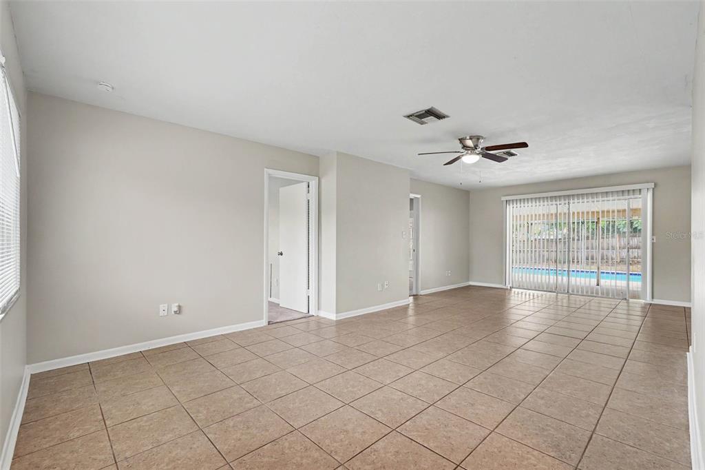 An empty living room with beige tile flooring, a ceiling fan, and sliding glass doors — 7170 HOLIDAY DRIVE, SPRING HILL, FL