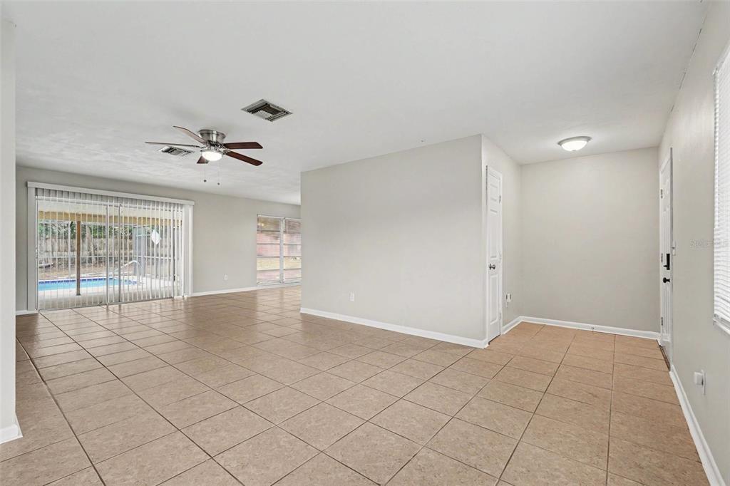 An open living area with beige tile flooring, a ceiling fan, and sliding glass patio doors — 7170 HOLIDAY DRIVE, SPRING HILL, FL