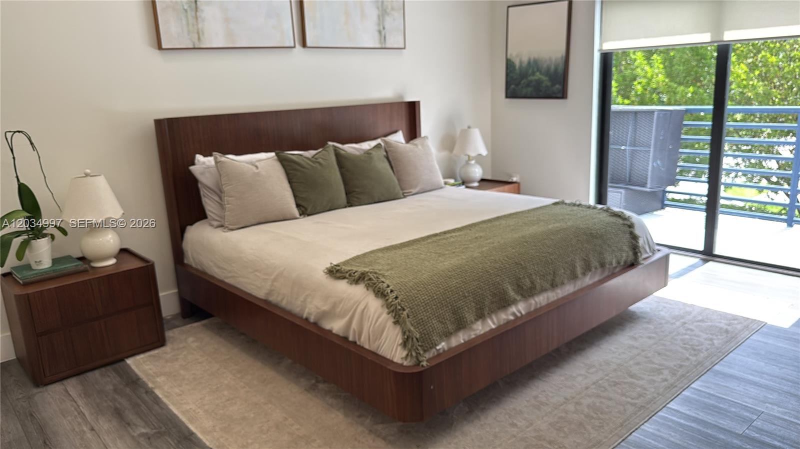 A modern bedroom features a wooden platform bed, neutral bedding, and a sliding glass door — 21251 NE 3rd Ct, Miami FL 33179, MIAMI, FL