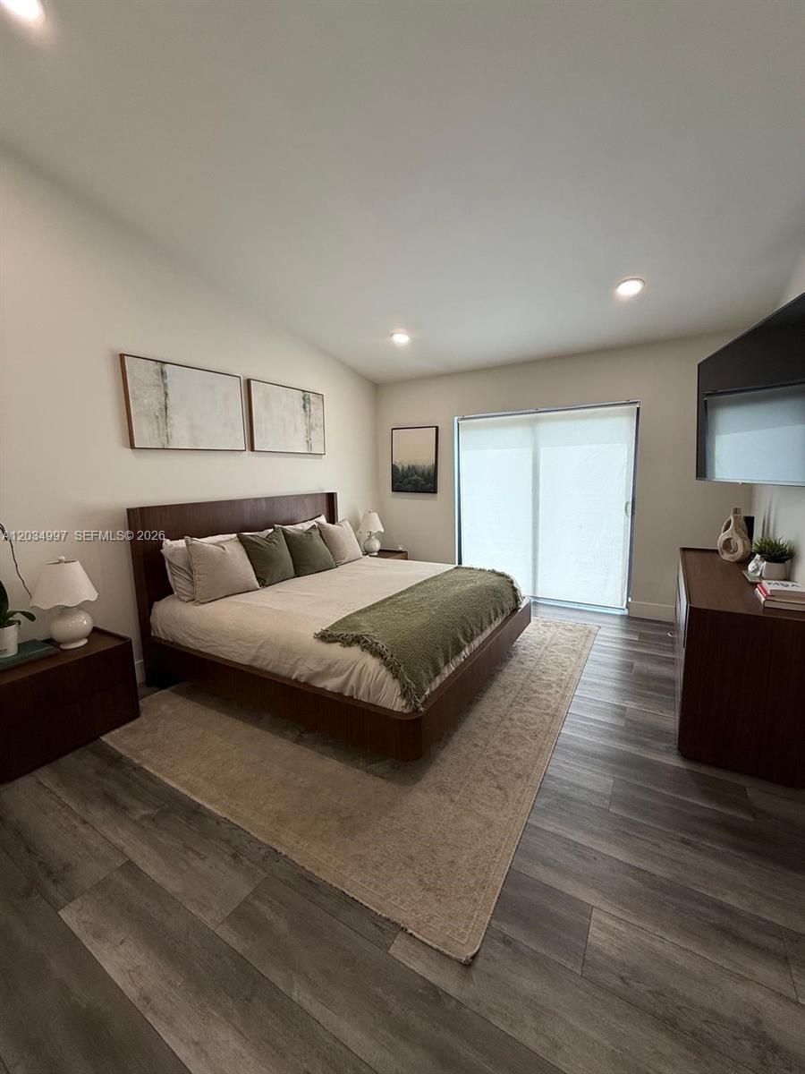 A bedroom features a wooden bed frame, neutral bedding, a rug, and sliding glass doors — 21251 NE 3rd Ct, Miami FL 33179, MIAMI, FL