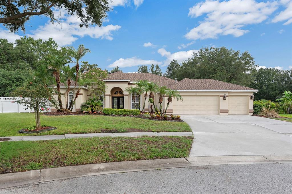 A single-story house with a beige stucco exterior, a three-car garage, and palm trees — 5711 TANAGERSIDE ROAD, LITHIA, FL