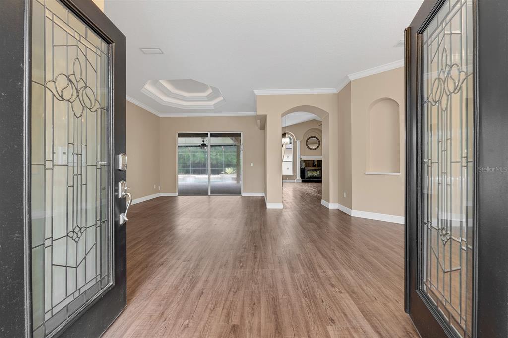 An entryway opens into a living area with wood-look flooring and a tray ceiling — 5711 TANAGERSIDE ROAD, LITHIA, FL