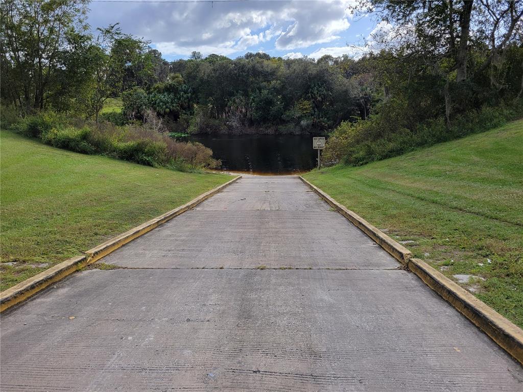 A concrete boat ramp leads down into a dark pond surrounded by trees and grass — SE 74TH LANE ROAD UNIT 6-EAST, OCKLAWAHA, FL