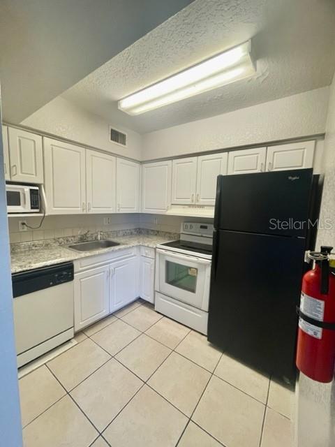 A kitchen features white cabinets, granite countertops, a black refrigerator, and a tiled floor — 730 WYMAN COURT UNIT 730, ORLANDO, FL