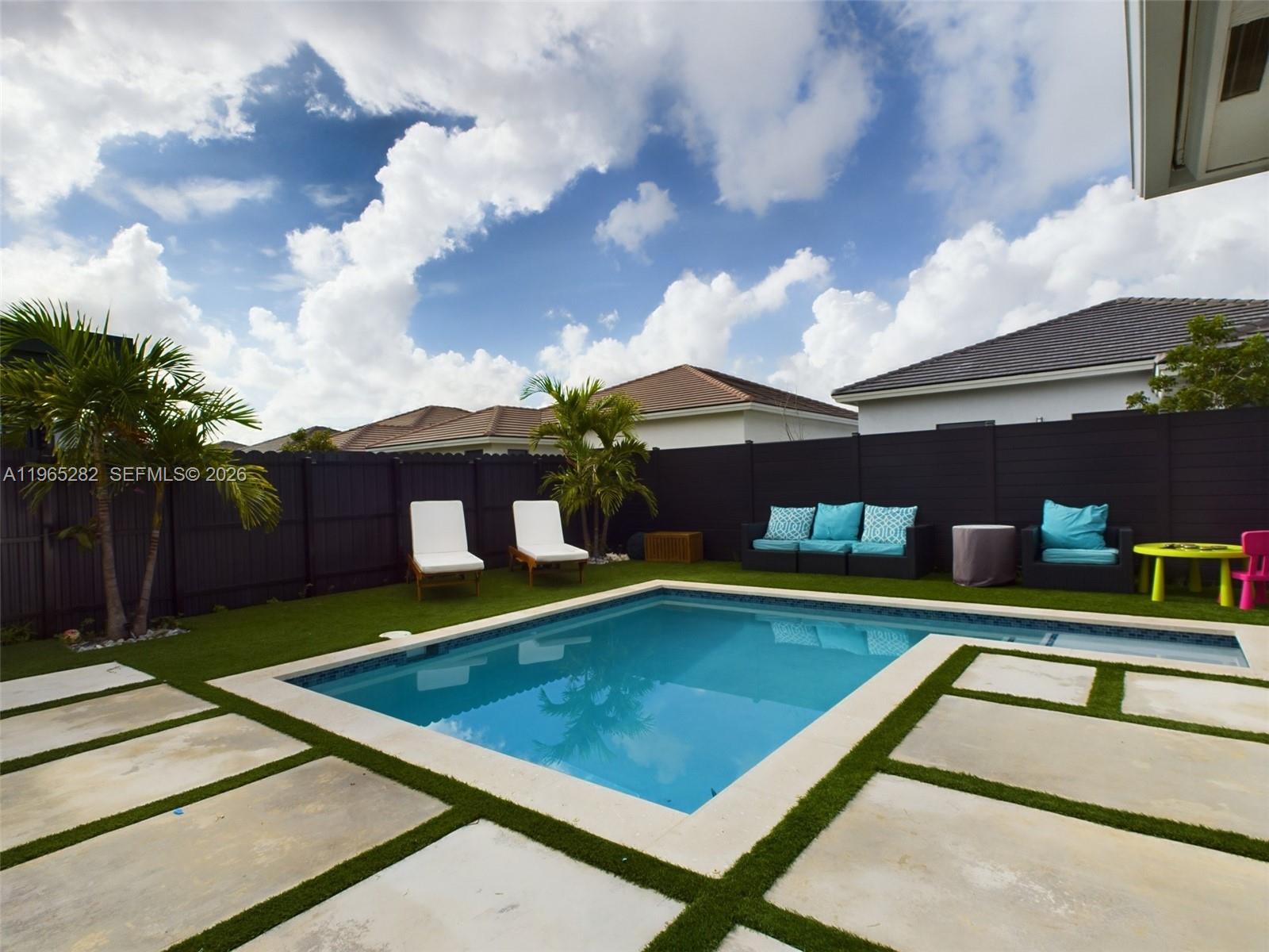 A backyard features a rectangular swimming pool, lounge chairs, patio furniture, and a black fence — 14560 SW 22nd Ter, Miami FL 33175, MIAMI, FL