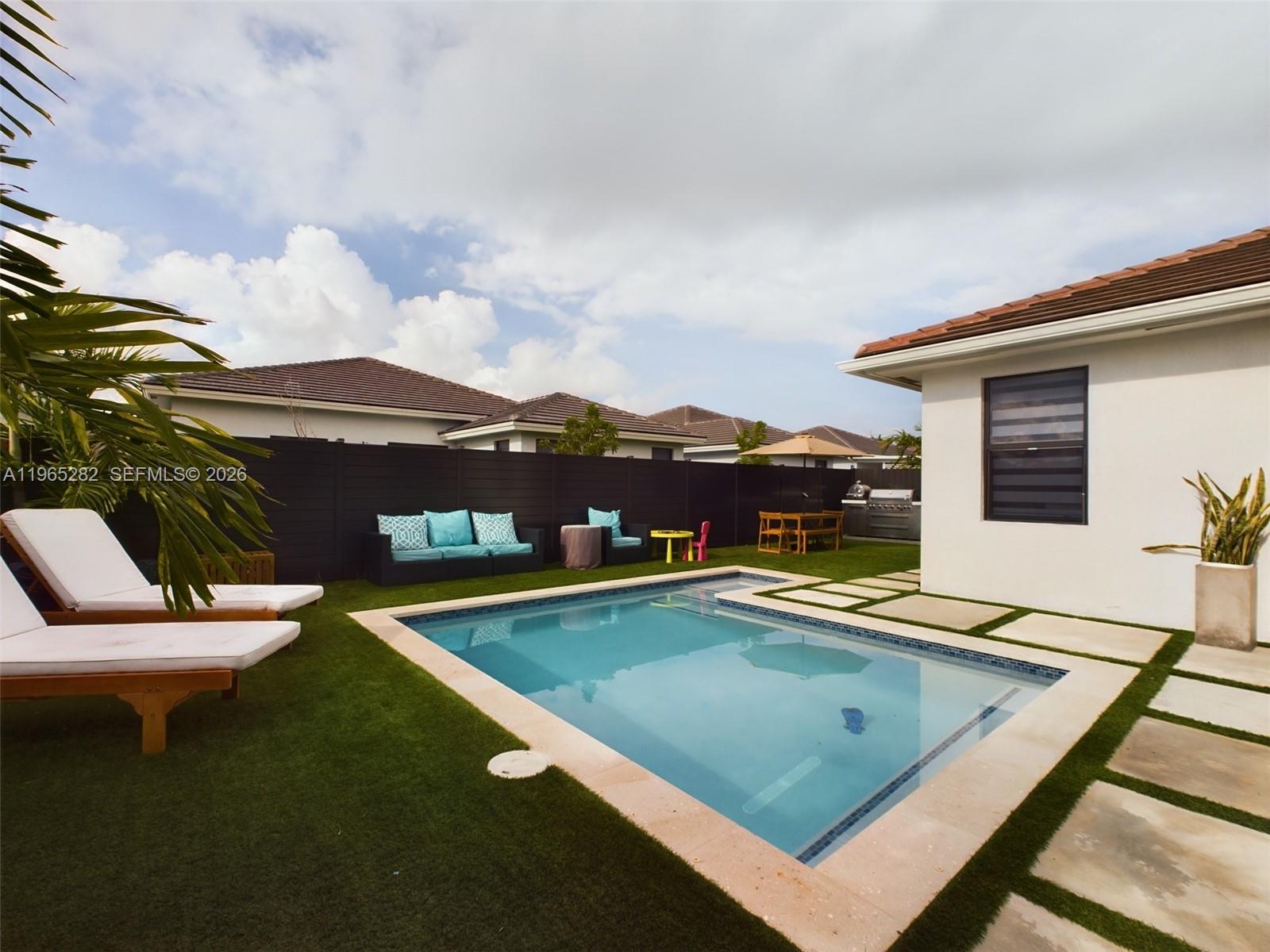 A backyard features a rectangular swimming pool, artificial turf, lounge chairs, and a patio area — 14560 SW 22nd Ter, Miami FL 33175, MIAMI, FL