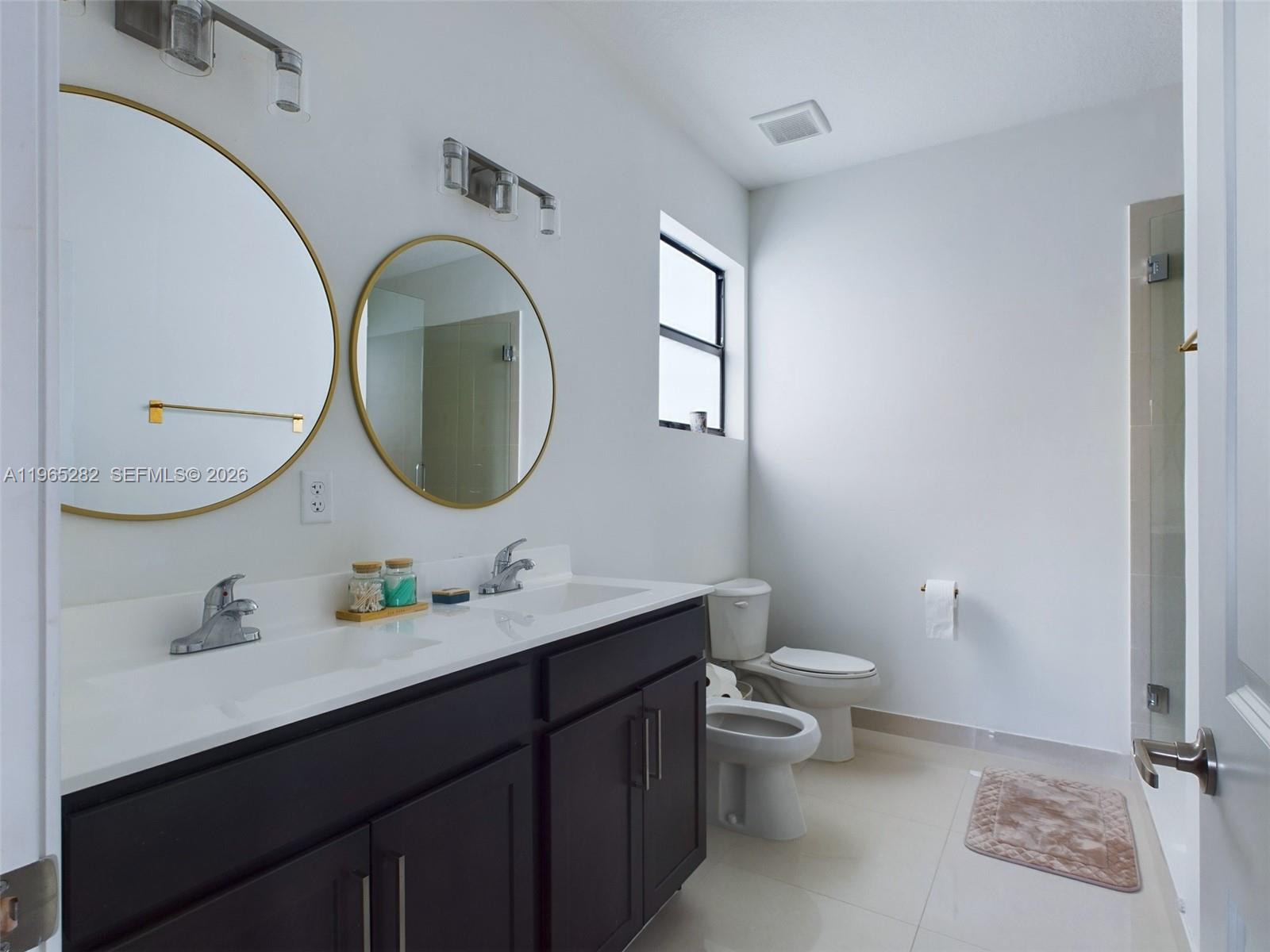 A modern bathroom features a double vanity with dark cabinets, gold-rimmed mirrors, and a shower — 14560 SW 22nd Ter, Miami FL 33175, MIAMI, FL