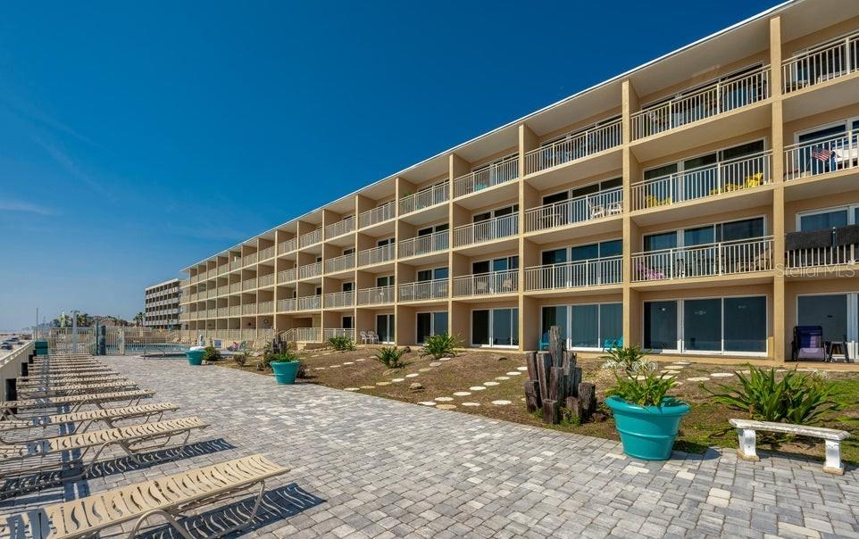 A multi-story apartment building with balconies overlooks a paved patio area with lounge chairs — 219 S ATLANTIC AVENUE UNIT 403, DAYTONA BEACH, FL