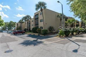 A three-story apartment building with tan stucco siding and palm trees in the parking lot — 11485 OAKHURST ROAD UNIT 200-318, LARGO, FL