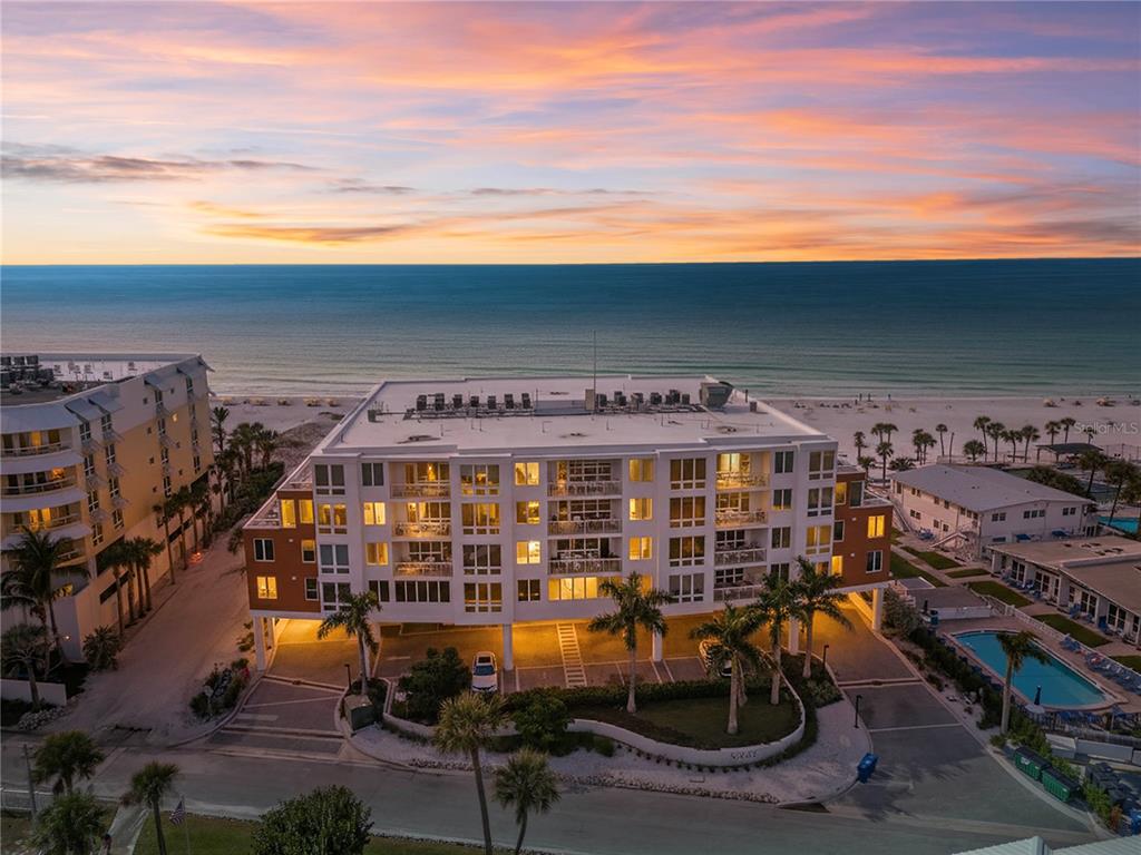 An aerial view of a multi-story beachfront condominium building at sunset with palm trees below — 1035 SEASIDE DRIVE UNIT 404, SARASOTA, FL