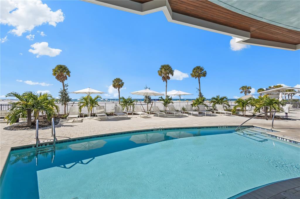 A swimming pool sits on a patio overlooking a sandy beach with palm trees — 1035 SEASIDE DRIVE UNIT 404, SARASOTA, FL