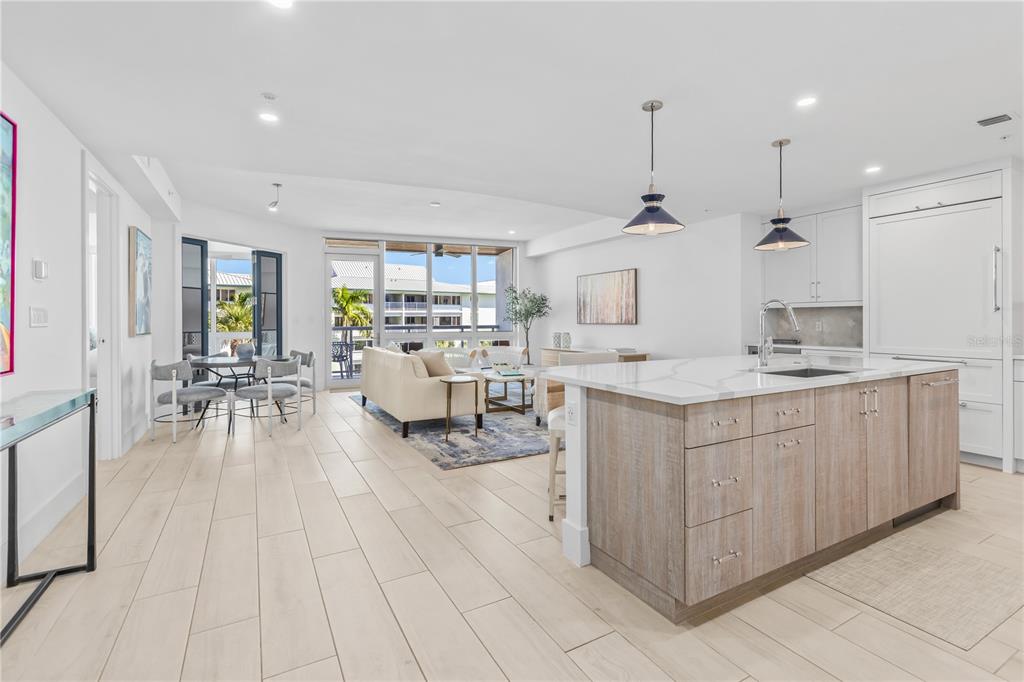 An open-concept kitchen and living area features light wood flooring, a large island, and balcony — 1035 SEASIDE DRIVE UNIT 404, SARASOTA, FL