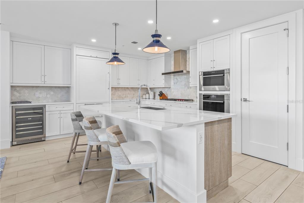 A modern kitchen features white cabinetry, a marble-topped island with seating, and stainless steel appliances — 1035 SEASIDE DRIVE UNIT 404, SARASOTA, FL