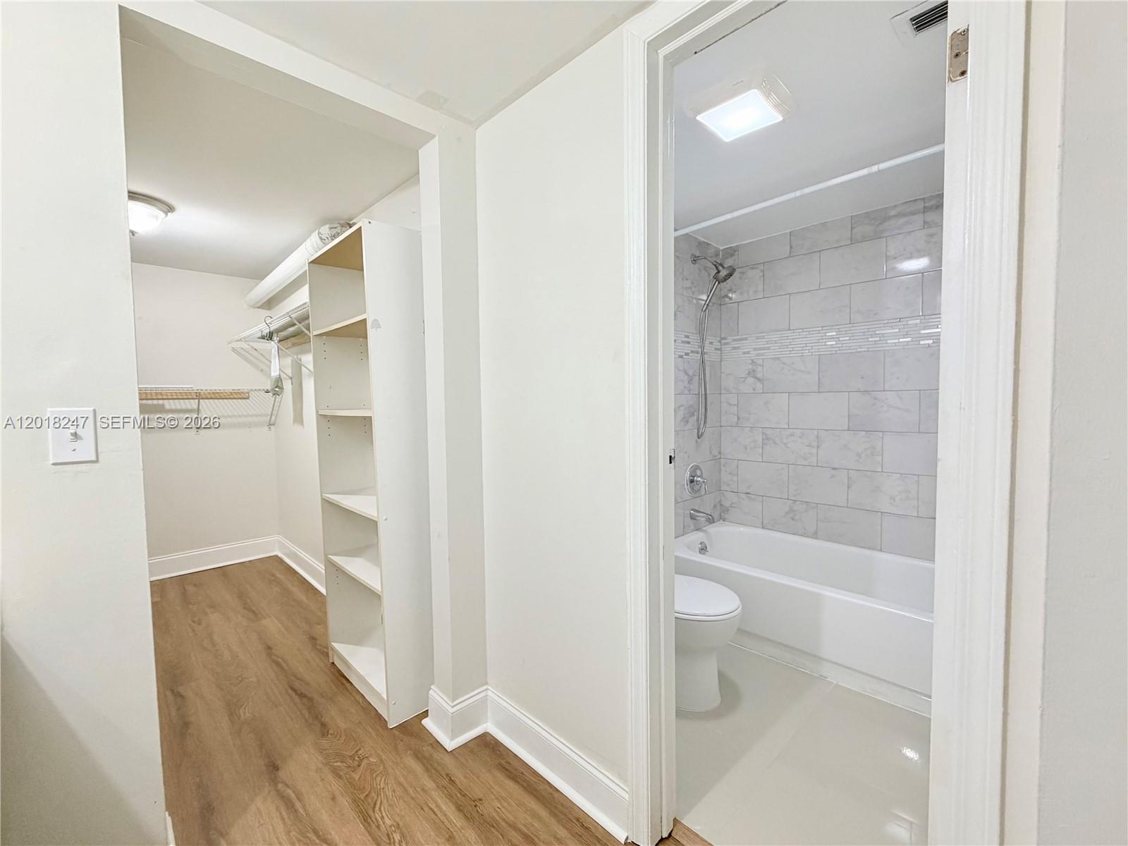 A walk-in closet with shelving sits adjacent to a bathroom featuring a tiled tub shower — 450 Commodore Dr # 214, Plantation FL 33325, PLANTATION, FL