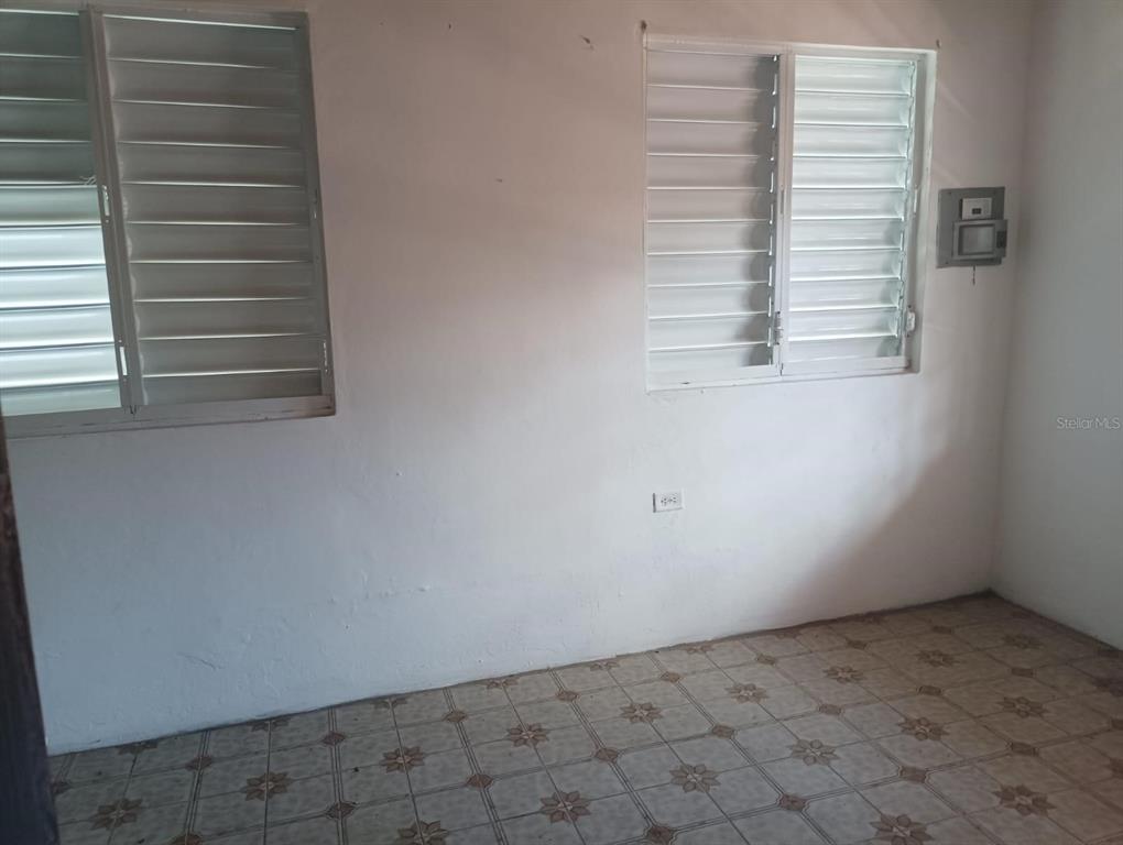 An empty room features white walls, tiled flooring, and two louvered windows — Galniel #A44 BARRIADA GARNIER, MAYAGUEZ, PR