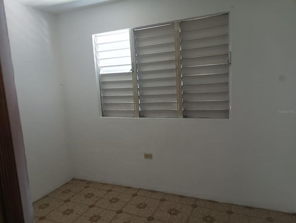 An empty room features white walls, a tiled floor, and a large louvered window — Galniel #A44 BARRIADA GARNIER, MAYAGUEZ, PR