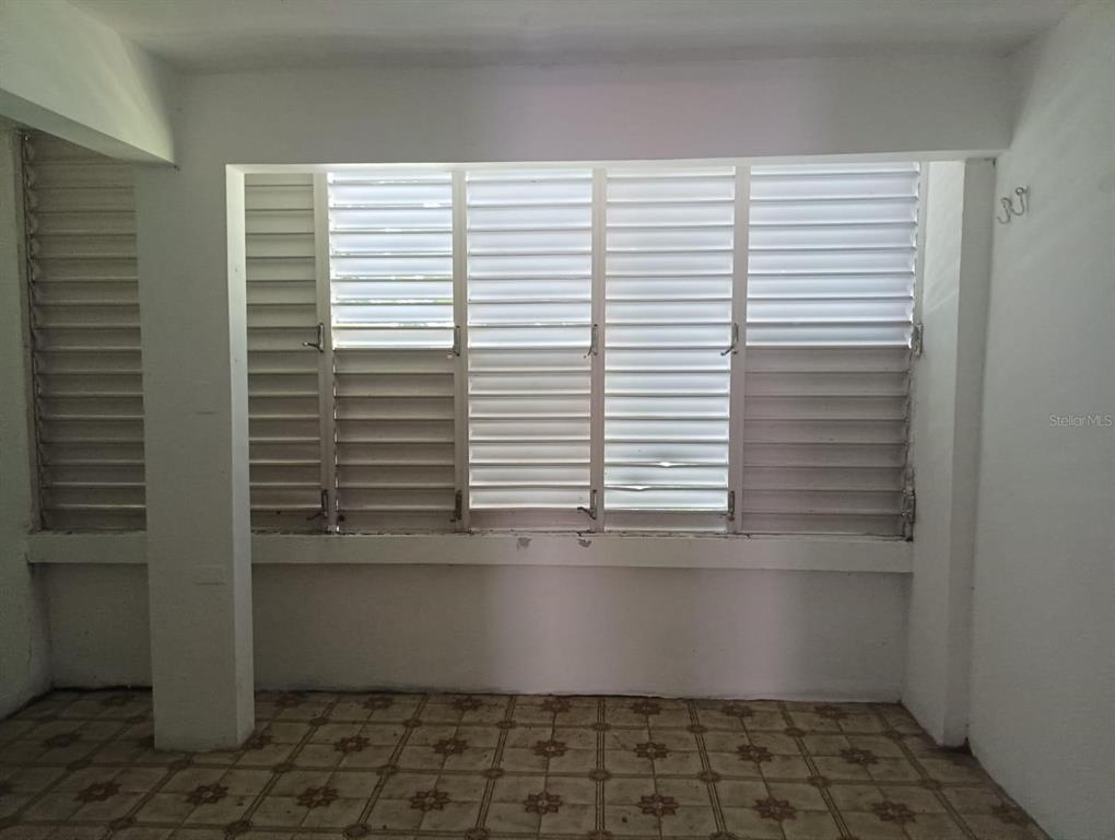 A room with tiled flooring and a large wall of white louvered windows — Galniel #A44 BARRIADA GARNIER, MAYAGUEZ, PR