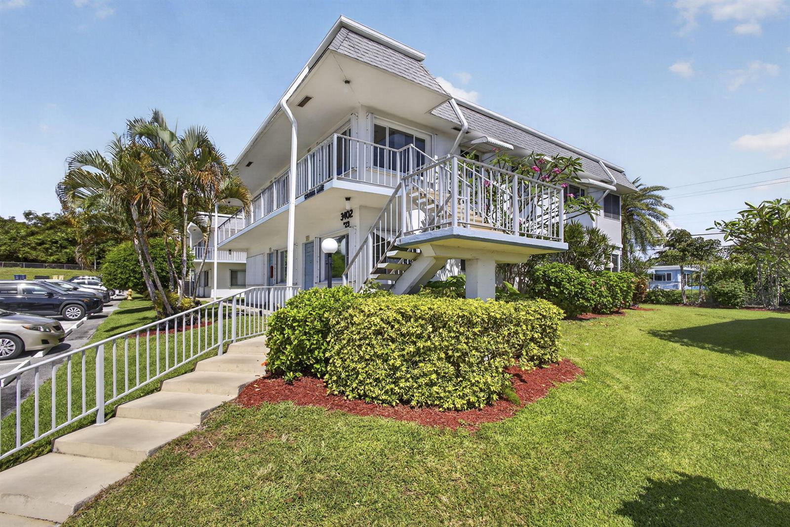 A two-story apartment building features a white exterior, a metal staircase, and a landscaped lawn — 3402 Cynthia Lane # 201, FL 33461, FL