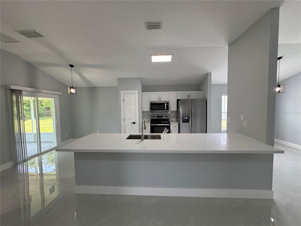 A kitchen features a large white quartz island, stainless steel appliances, and light gray walls — 12 REYNOLDS PLACE, PALM COAST, FL
