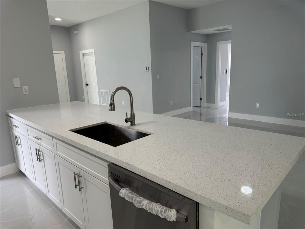 A kitchen island with a white speckled countertop, stainless steel sink, and white cabinets — 12 REYNOLDS PLACE, PALM COAST, FL