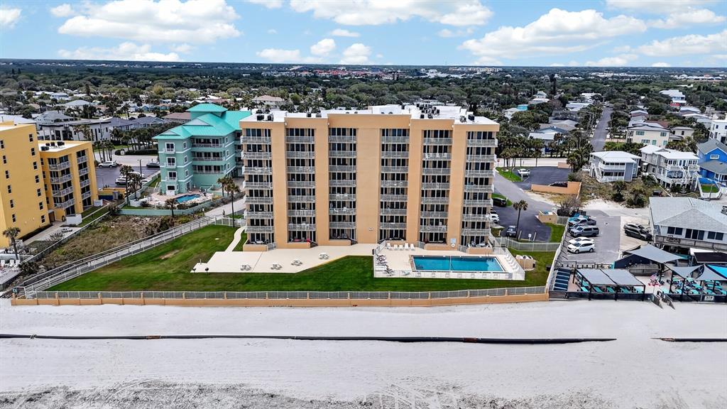 An aerial view shows a tan multi-story condominium building with a pool near a beach — 421 S ATLANTIC AVENUE UNIT 409, NEW SMYRNA BEACH, FL