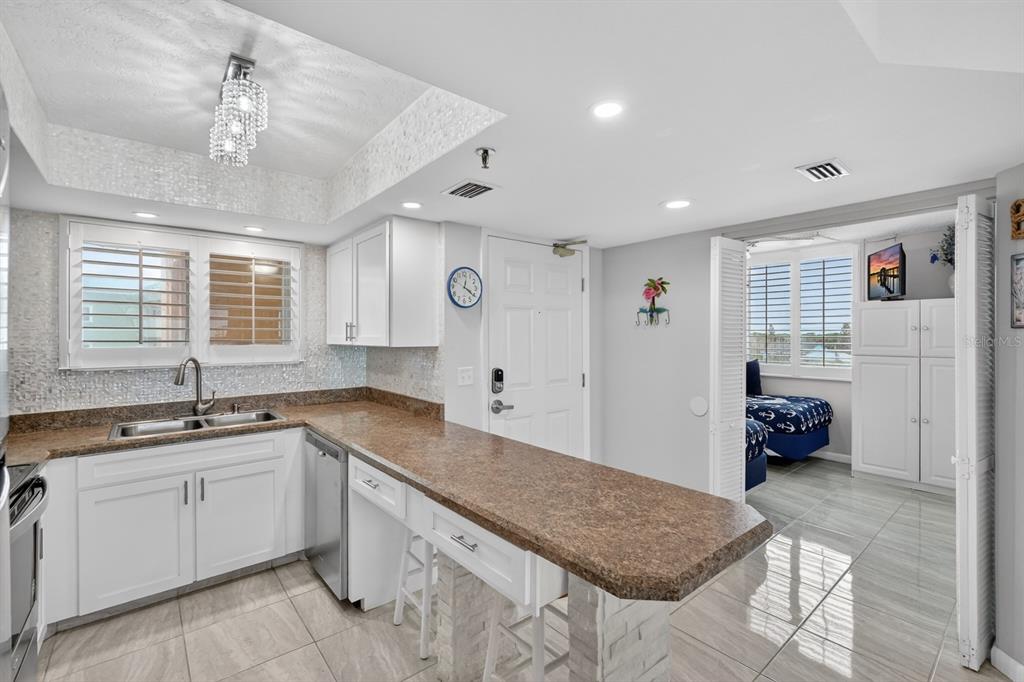A kitchen with white cabinets, granite countertops, and tile flooring opens into an adjacent bedroom — 421 S ATLANTIC AVENUE UNIT 409, NEW SMYRNA BEACH, FL