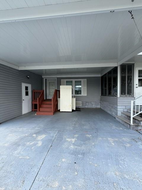 A covered concrete carport features gray siding, a white door, and a set of wooden stairs — 194 ROSEWOOD DRIVE, COCOA, FL