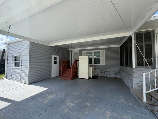 A covered carport area features a concrete floor, gray siding, and a set of wooden stairs — 194 ROSEWOOD DRIVE, COCOA, FL