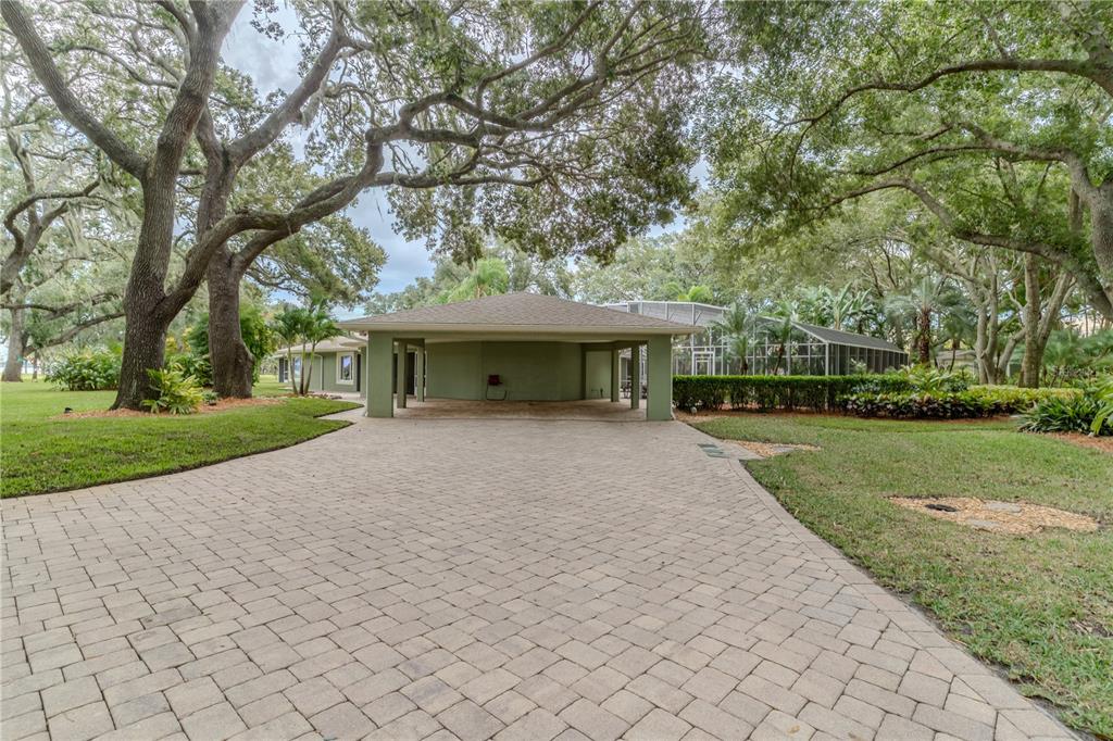 A paved driveway leads to a covered carport attached to a house under large trees — 8010 LAKE LOWERY ROAD, HAINES CITY, FL
