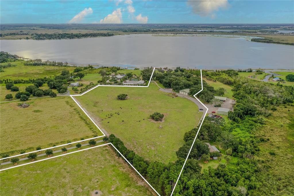 An aerial view shows a large, fenced grassy pasture bordering a lake with several buildings — 8010 LAKE LOWERY ROAD, HAINES CITY, FL