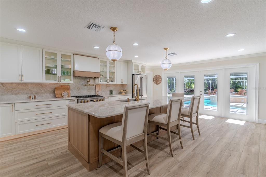 A kitchen features white cabinetry, a wood-toned island with seating, and glass doors overlooking a pool — 8010 LAKE LOWERY ROAD, HAINES CITY, FL