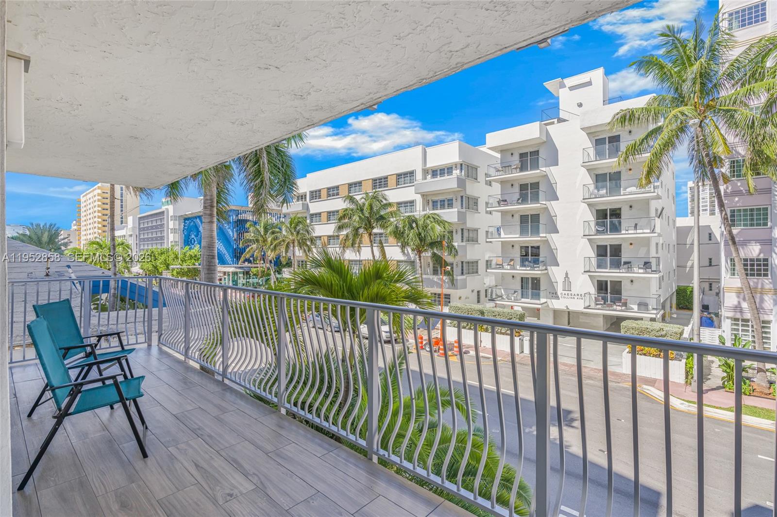A balcony with two teal chairs overlooks a street and nearby white apartment buildings — 4141 Collins Ave # 201, Miami Beach FL 33140, MIAMI BEACH, FL