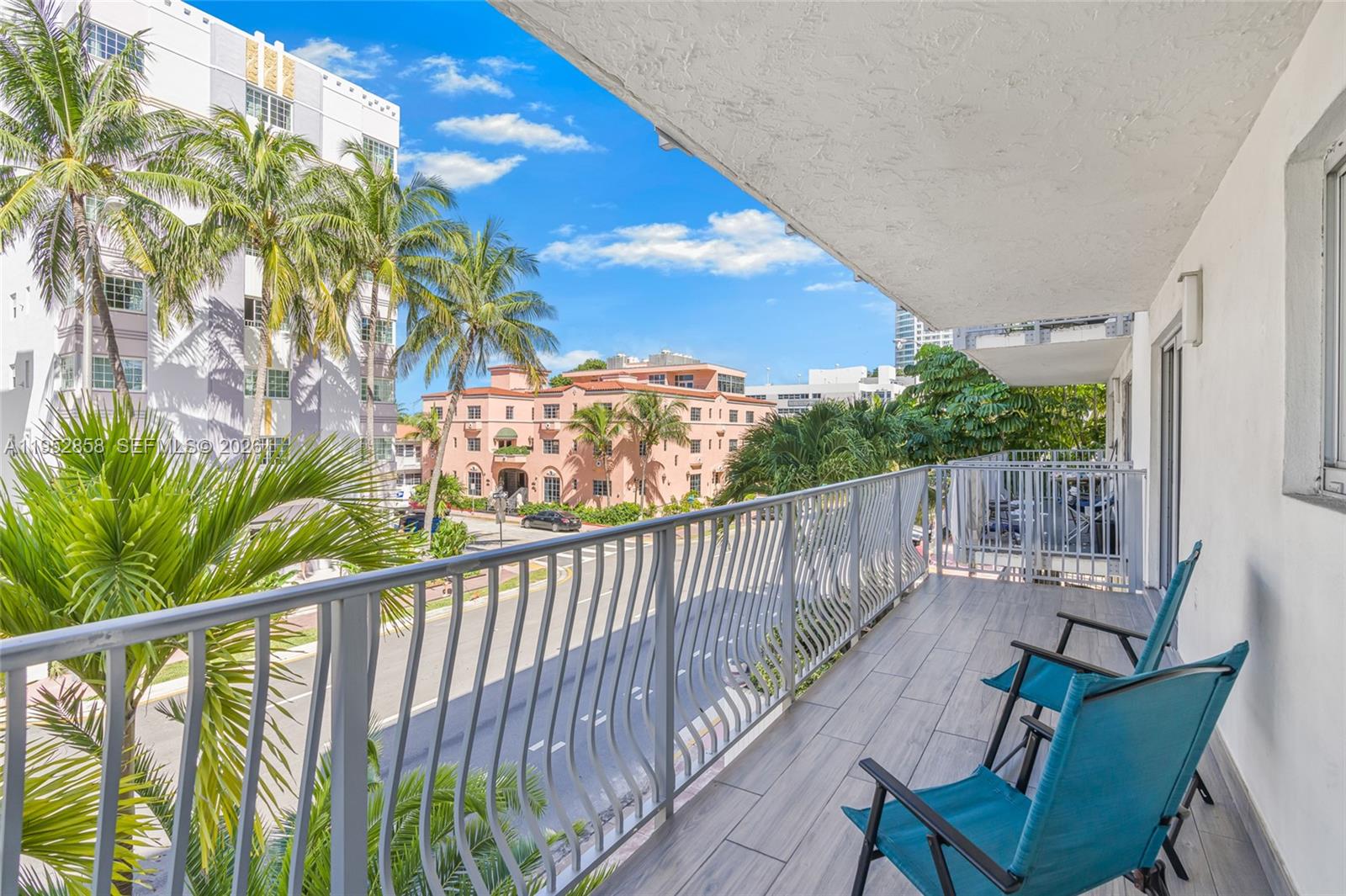 A balcony with gray wood-look flooring and two blue chairs overlooks a street and buildings — 4141 Collins Ave # 201, Miami Beach FL 33140, MIAMI BEACH, FL