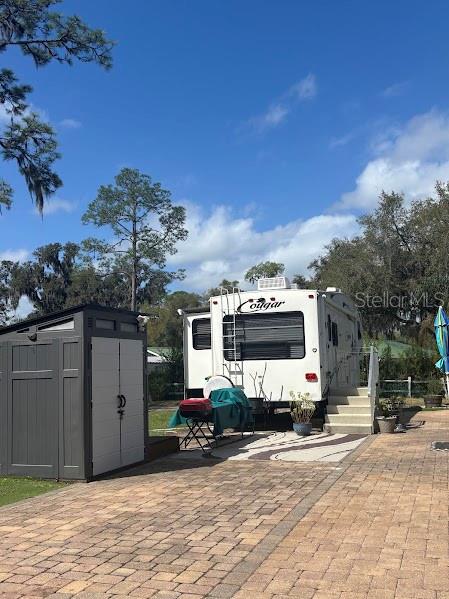 A white Cougar travel trailer is parked on a paved lot next to a storage shed — 14114 252ND TERRACE ROAD NE LOT 12, FORT MC COY, FL