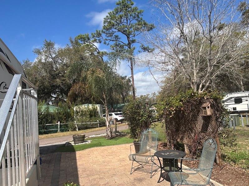 A paved patio features two metal chairs and a small table beside a vine-covered structure — 14114 252ND TERRACE ROAD NE LOT 12, FORT MC COY, FL