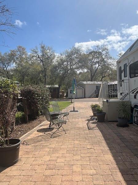 A paved patio area features outdoor chairs, potted plants, and a view of neighboring homes — 14114 252ND TERRACE ROAD NE LOT 12, FORT MC COY, FL