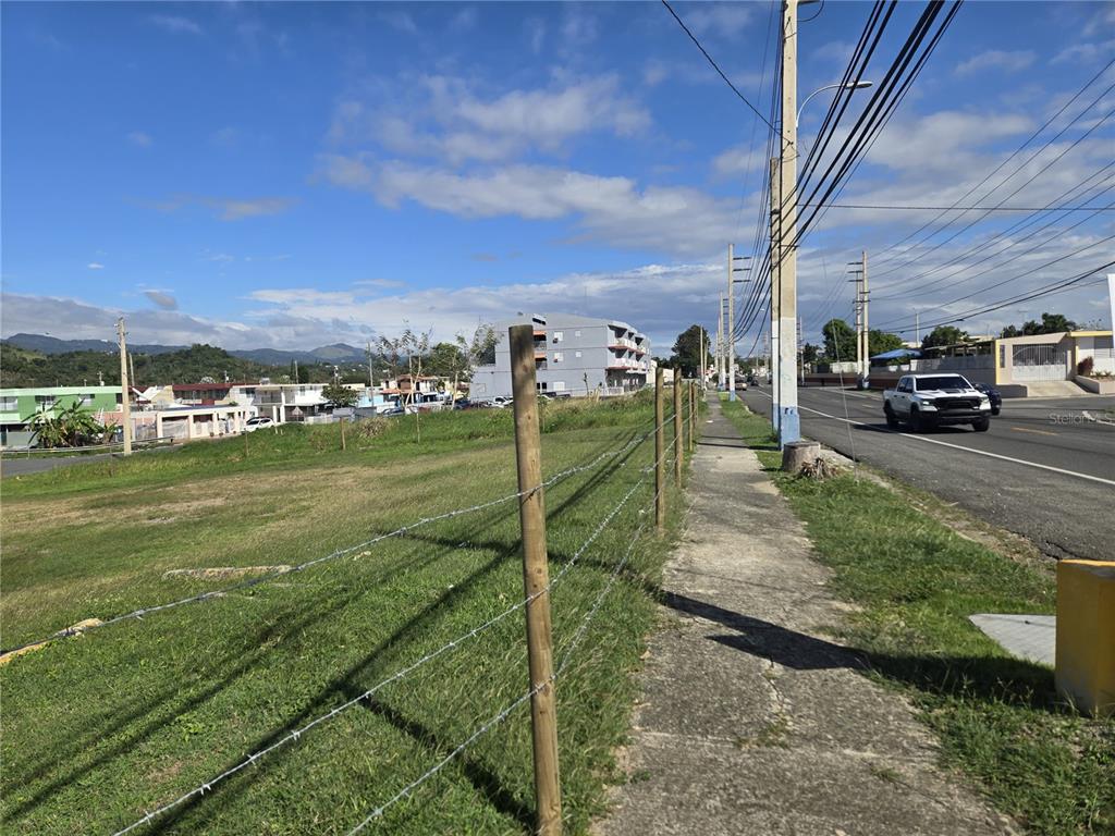 A grassy vacant lot sits beside a sidewalk and a road with a white truck — 102 carr AVE. UNIVERSIDAD INTERAMERICANA, SAN GERMAN, PR