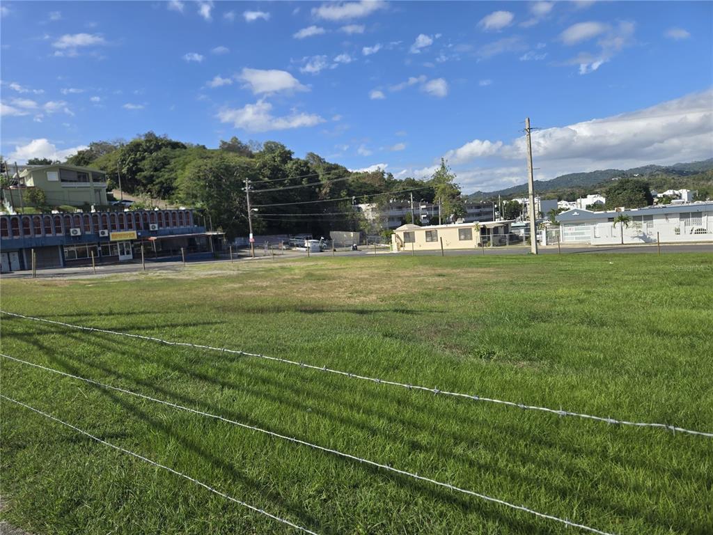 A large, grassy vacant lot is enclosed by a barbed wire fence under a blue sky — 102 carr AVE. UNIVERSIDAD INTERAMERICANA, SAN GERMAN, PR