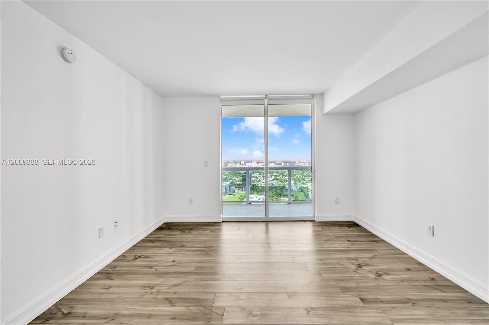 An empty room features white walls, wood-look flooring, and a sliding glass door to a balcony — 1800 N Bayshore Dr # 4208, Miami FL 33132, MIAMI, FL