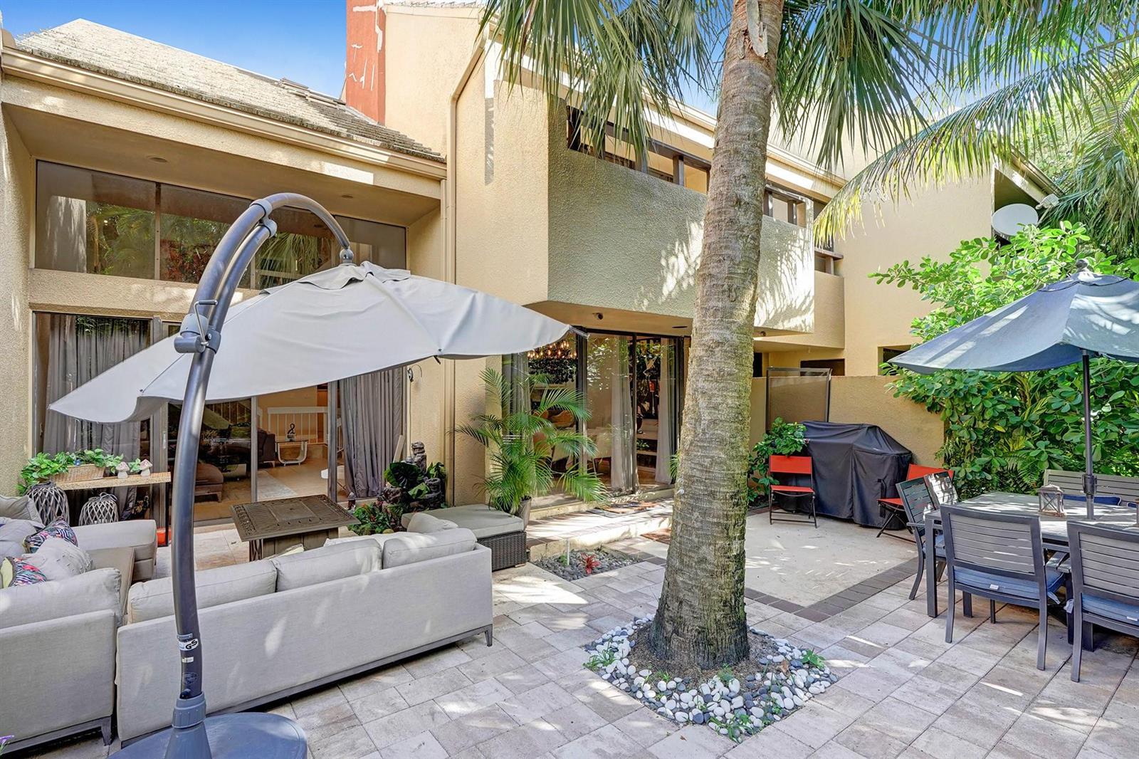 A paved patio features a palm tree, outdoor seating, a dining set, and umbrellas — 702 Saint Albans Drive # 702, Boca Raton FL 33486, BOCA RATON, FL