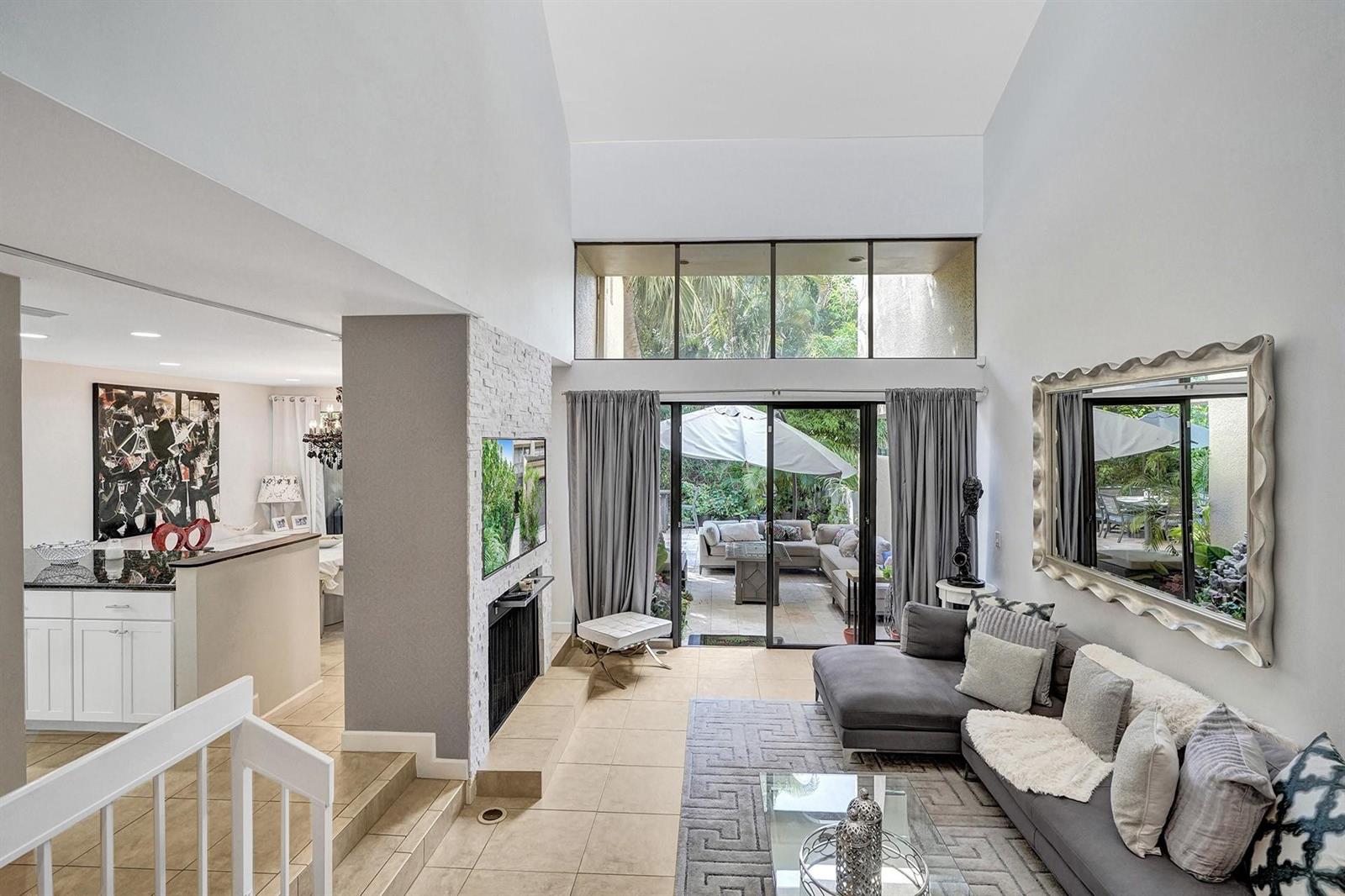 A living room with a stone fireplace, high ceilings, and sliding doors leading to a patio — 702 Saint Albans Drive # 702, Boca Raton FL 33486, BOCA RATON, FL