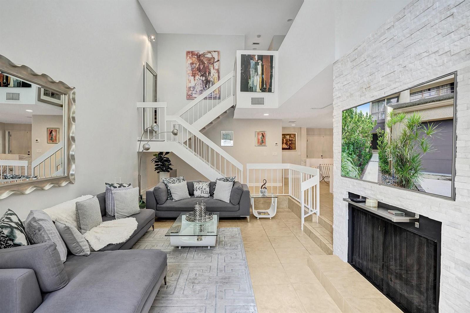 A living room features a fireplace, a staircase, gray sofas, and a large wall mirror — 702 Saint Albans Drive # 702, Boca Raton FL 33486, BOCA RATON, FL