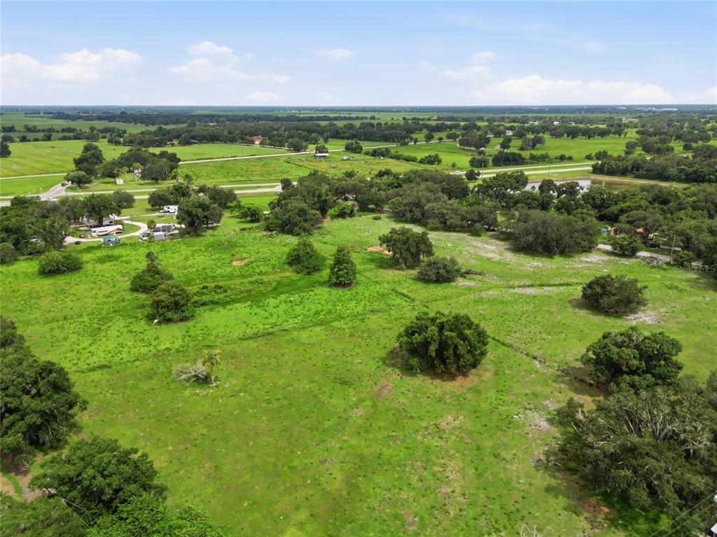 An aerial view shows a large, grassy pasture with scattered trees and a distant road — 1823 NE HAMMOCK STREET, ARCADIA, FL