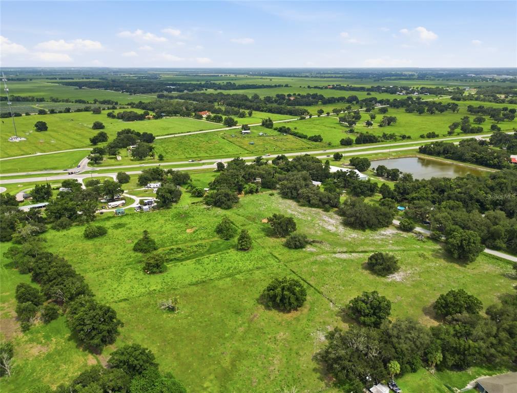 An aerial view shows a large, grassy rural property with scattered trees and a pond — 1823 NE HAMMOCK STREET, ARCADIA, FL