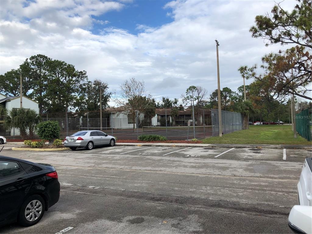 A fenced tennis court sits behind a parking lot with several cars parked nearby — 2616 LEMON TREE LANE UNIT F, ORLANDO, FL