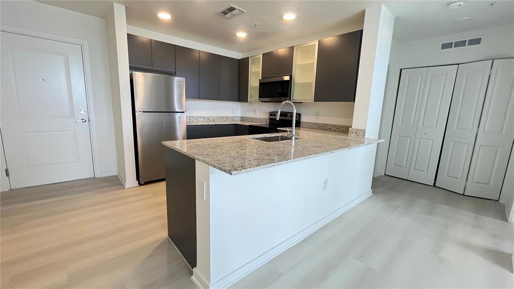 A kitchen features dark cabinetry, stainless steel appliances, and a granite-topped island with a sink — 5579 MILLENIA PARK BOULEVARD UNIT 502, ORLANDO, FL