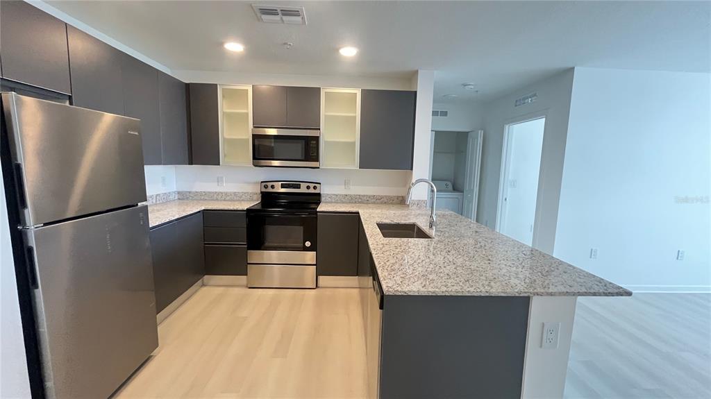 A modern kitchen features dark gray cabinetry, granite countertops, stainless steel appliances, and light flooring — 5579 MILLENIA PARK BOULEVARD UNIT 502, ORLANDO, FL