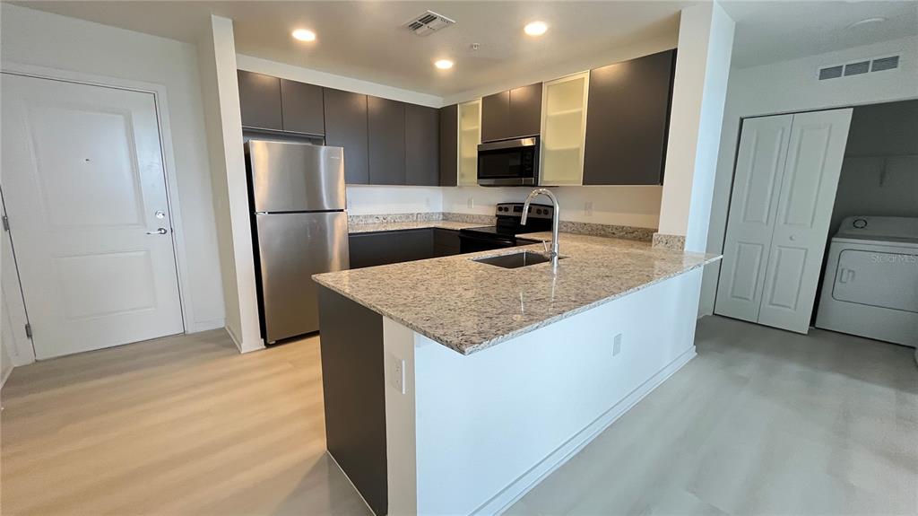 A kitchen features dark cabinetry, stainless steel appliances, and a granite-topped island with a sink — 5579 MILLENIA PARK BOULEVARD UNIT 502, ORLANDO, FL