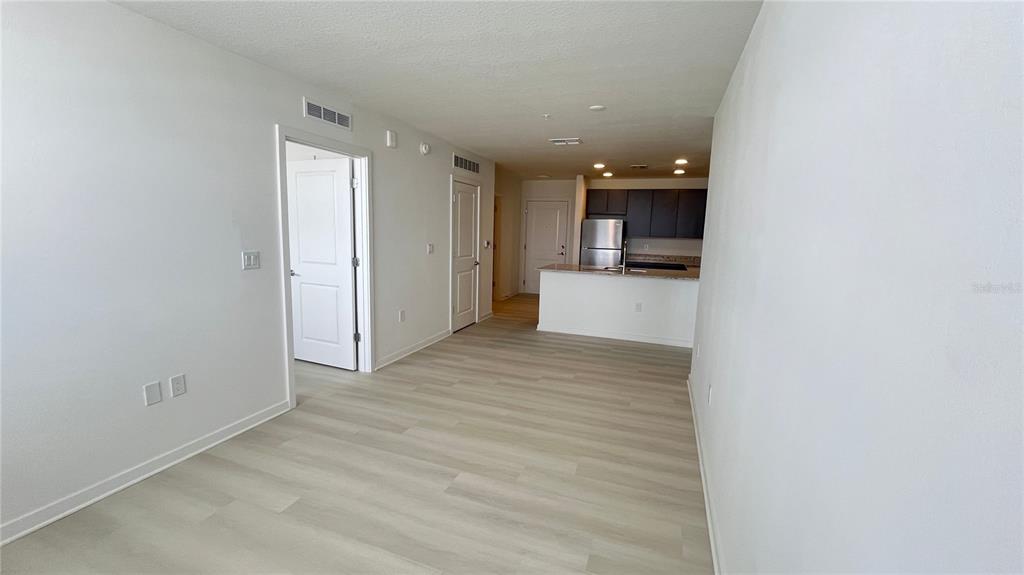 An open-concept living area features light wood-look flooring, white walls, and a kitchen with dark cabinets — 5579 MILLENIA PARK BOULEVARD UNIT 502, ORLANDO, FL